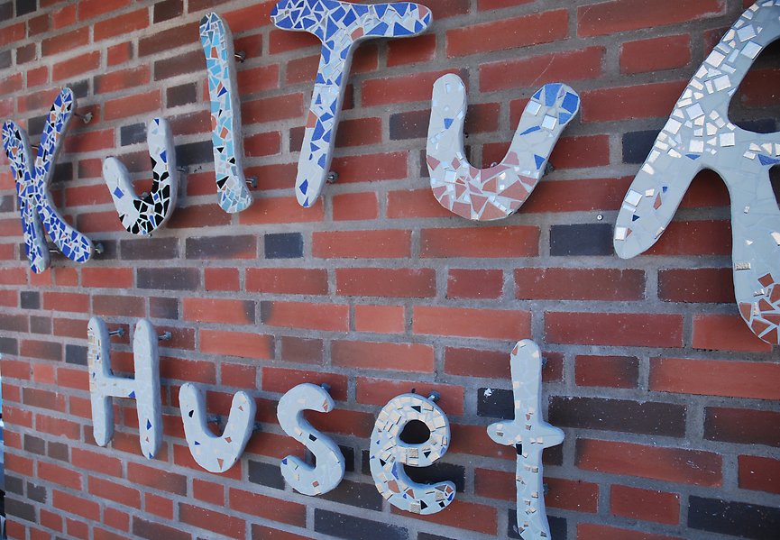 Foto på konstnärligt utformade bokstäver i mosaik på en tegelvägg. Bokstäverna på två rader bildar ordet Kulturhuset.