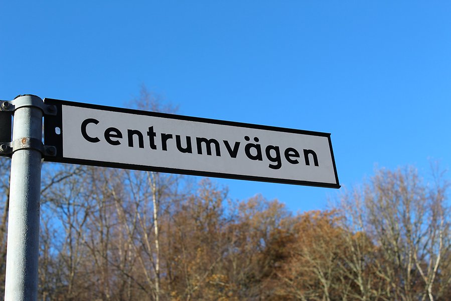 Bild på en vit gatusjykt med svart text som det står "Centrumvägen" på. I bakgrunden syns blå himmel.