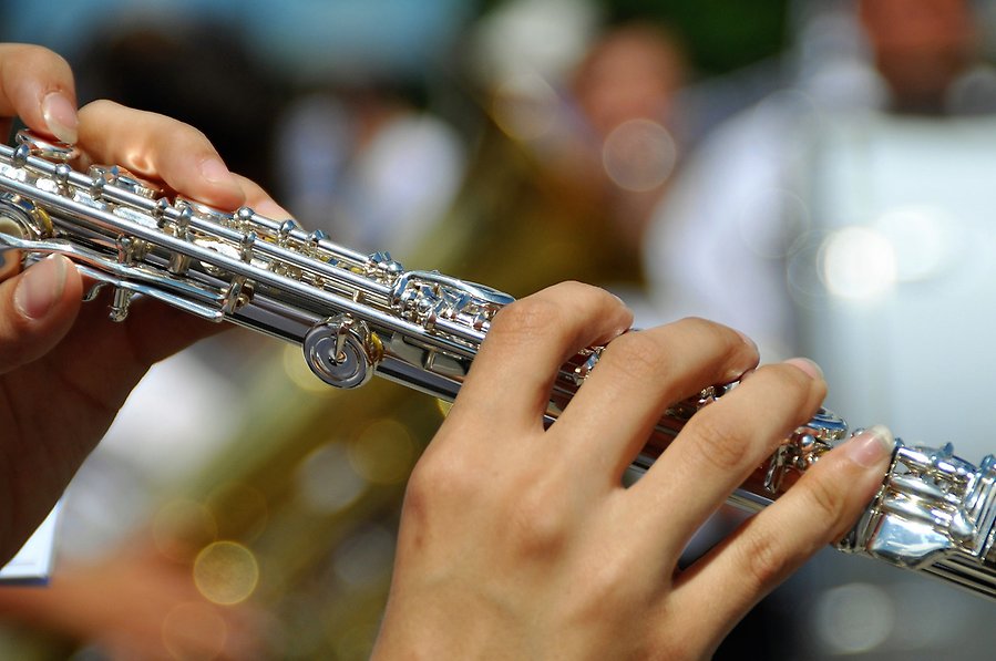 Bild på en person som spelar på en silvrig flöjt.