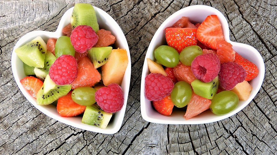Bild på frukt och bär i bitar i två hjärtformade skålar på en stubbe.