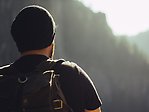 Bild på en person i mössa och t-shirt med ryggsäck som vandrar mot skogklädda berg.