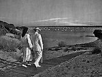 Gammal bild i svartvitt på ett par som promenerar mot en sandstrand.
