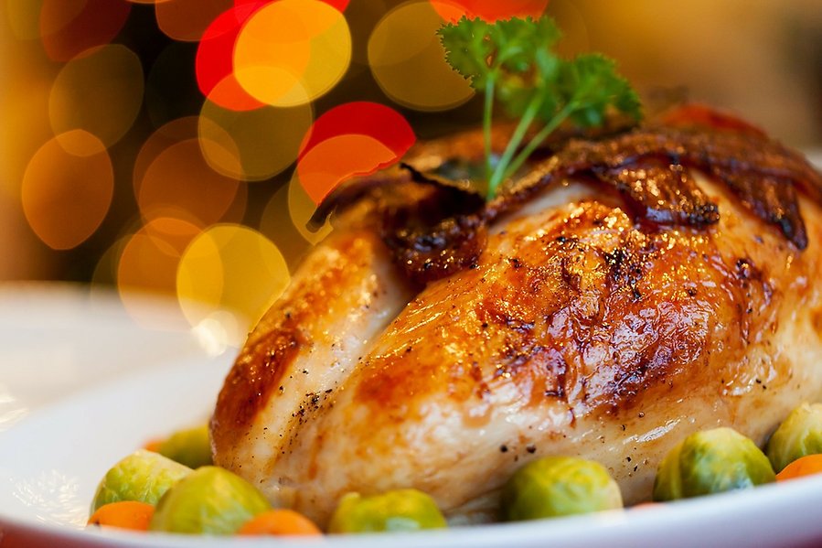 Foto på en ugnsstekt kyckling som ligger på en vit tallrik med grönsaker runt om. Skenet i fotot är varmt.