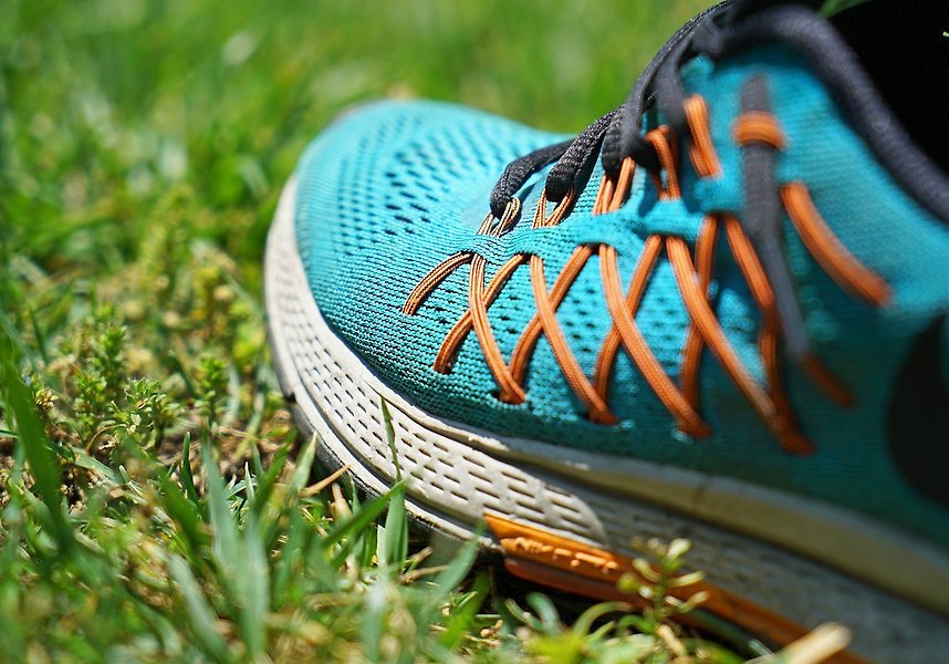 Foto på en joggingsko i klarblå färg med orangea snören. Skon står på en grön gräsmatta.