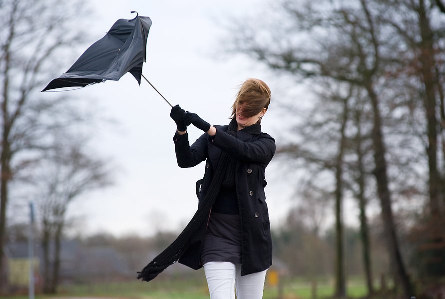 Person utomhus med paraply som viker sig i blåsten