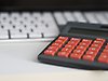 En miniräknare med röda knappar ligger framför ett tangentbord.