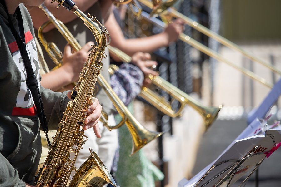 Närbild på barn som spelar saxofon, trumpeter och trombon. Endast armar och händer syns på barnen.