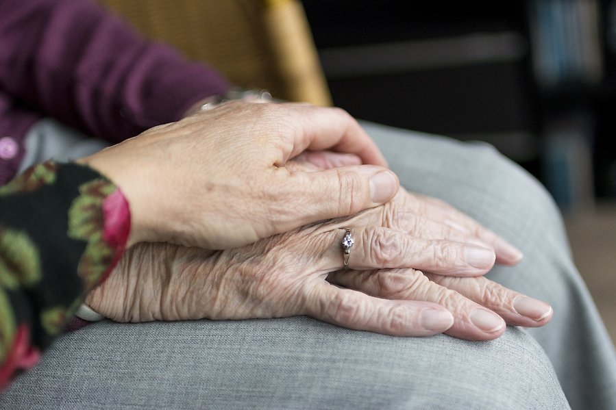 En person håller sin hand på en äldre persons händer.