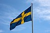 Svenska flaggan som är hissad i flaggstång en solig sommardag. 