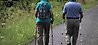 två äldre personer som går med stavar längst en grusväg.