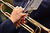 Foto på händer med röda naglar som spelar på en trumpet. På trumpeten sitter ett litet notställ med noter på.