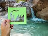Foto på en hand som håller i en illustration av en fabrik i grönt framför ett vattenfall.