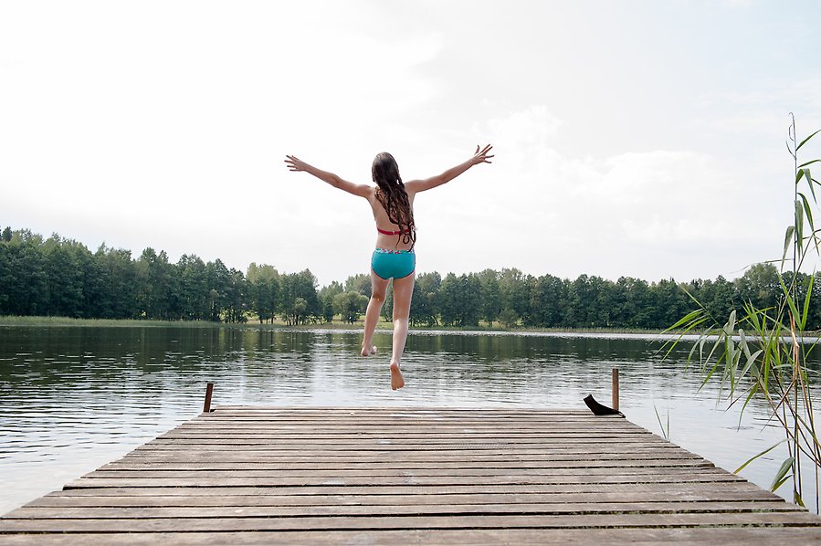 Flicka som hoppar från en brygga i en sjö.