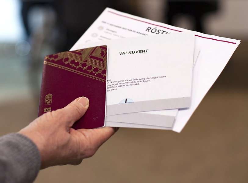 Hand som håller i pass, valsedlar och röstkort