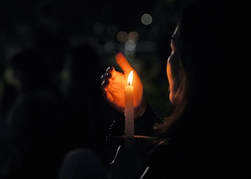 Mörk bild där en kvinna syns hålla en tänt ljus med en hand framför så att det inte ska blåsa ut. 