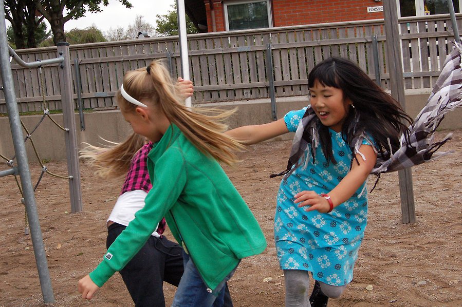 Bild på tre barn som springer runt en stolpe och skrattar och leker