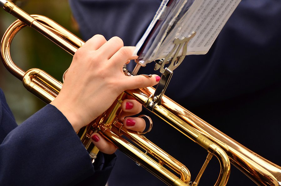 Foto på händer som spelar på en trumpet, naglarna är målade. På trumpeten sitter ett litet notställ.