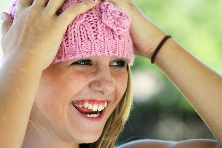 Närbild på en glad tjej som håller händerna utanpå sin rosa mössa.