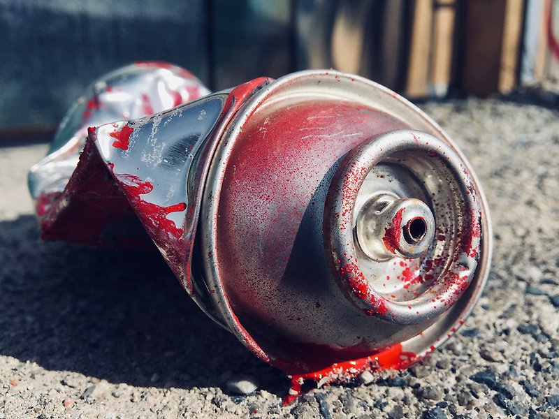 Foto på en tom, sönderknycklad, sprayburk med röd färg.