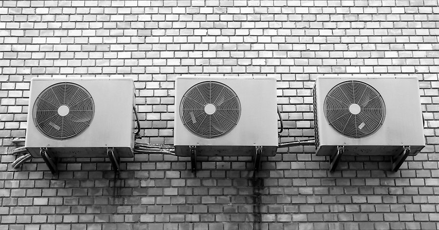 Foto på tre luftvärmepumpar med fläktar som sitter på en tegelvägg.