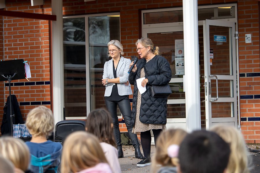 Två personer håller tal inför skolelever.
