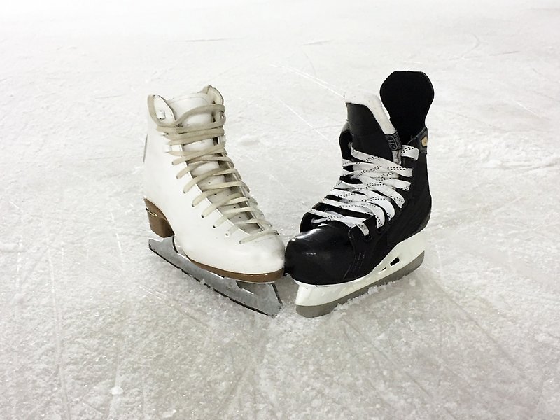 Foto på två skridskor på is, en vit konståkningsskridsko och en svart hockeyskridsko.