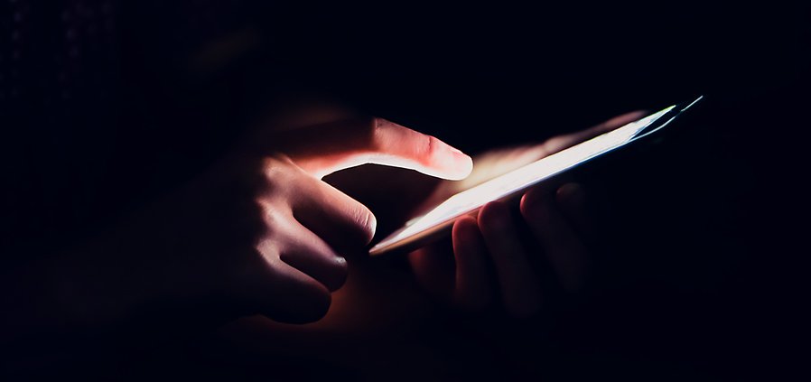 Bild på finger som trycker på en smartphone i mörk miljö