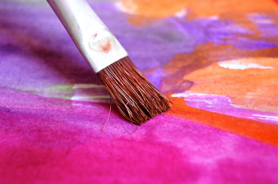 Foto på en akvarellpensel mot ett färgglatt papper i rosa, lila och orangea färger.