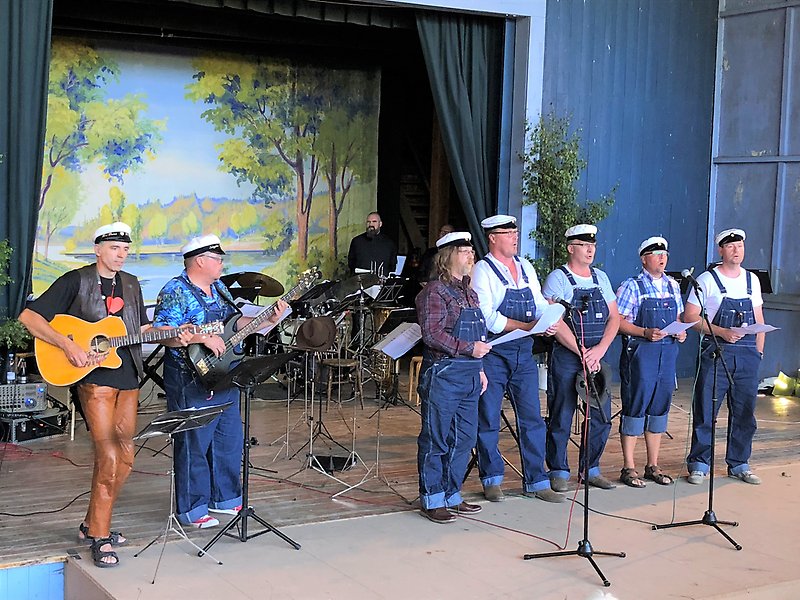 Foto på sju män som står på en scen och spelar och sjunger.