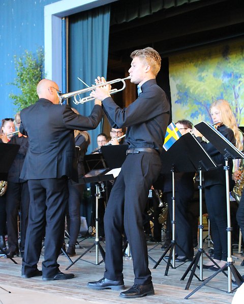 Foto på en ung man som spelar trumpet på en scen. I bakgrunden syns delar av en orkester.