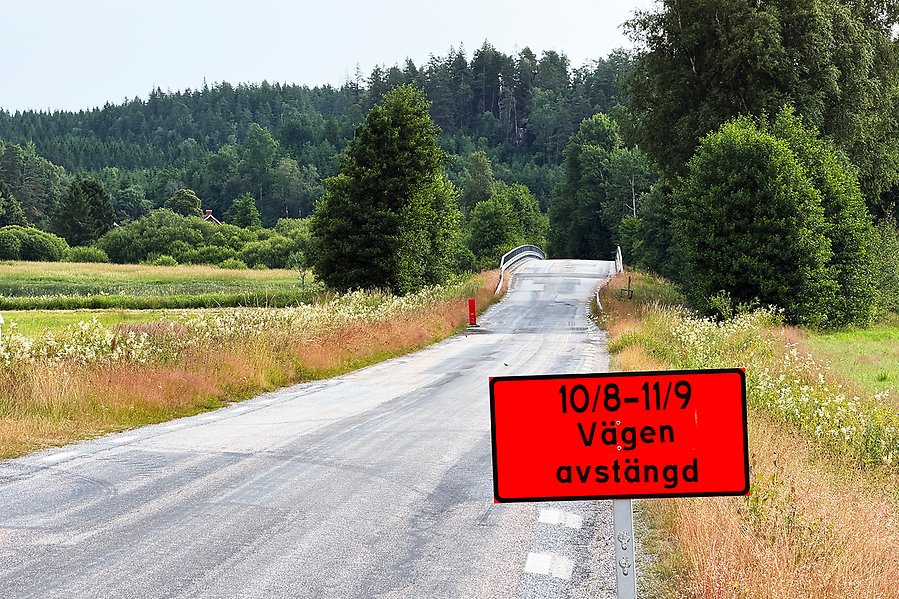 En väg som leder över en bro. I förgrunden en skylt med texten: Vägen avstängd