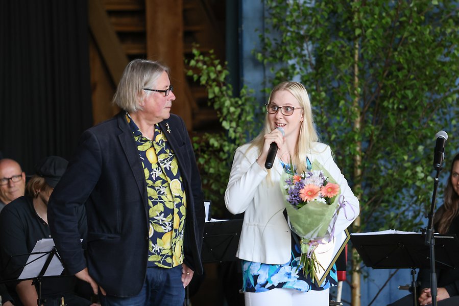 En man och en tjej som står på en scen. Tjejen har en blombukett i handen.