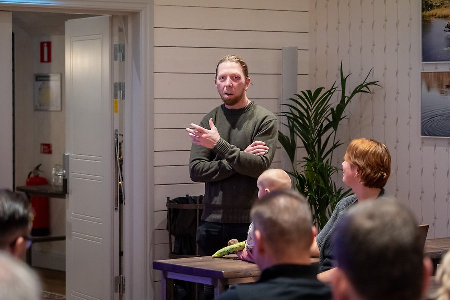 En person talar inför flera deltagare.
