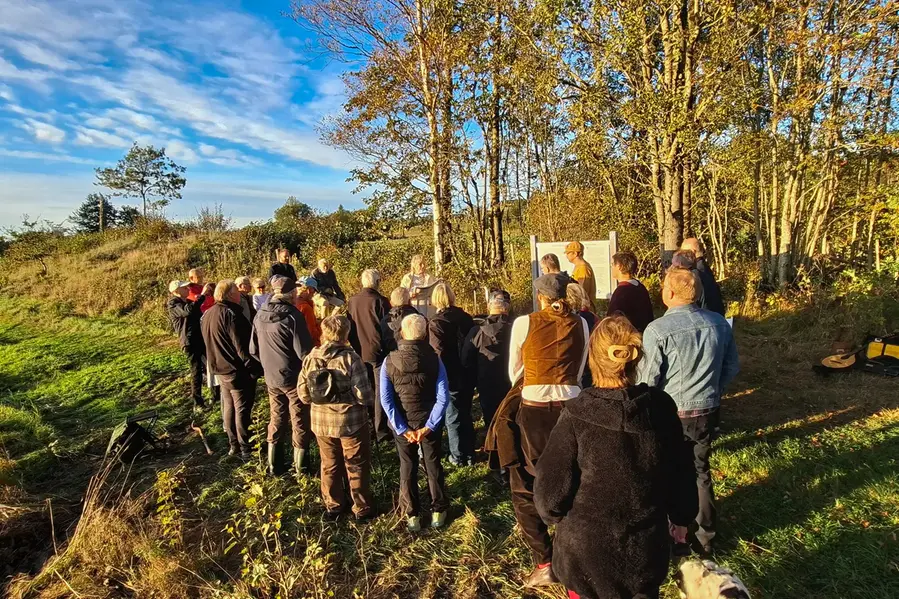 En grupp människor som står utomhus och lyssnar på en person som talar.