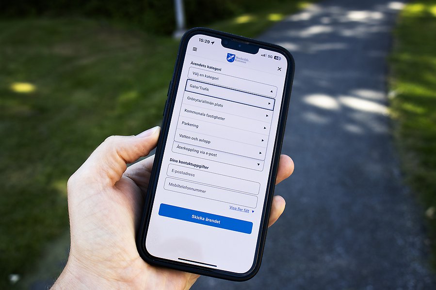 En hand som håller i en smartmobil. På skärmen syns en en app för att anmäla fel och brister på bland annat gator och vägar i kommunen.