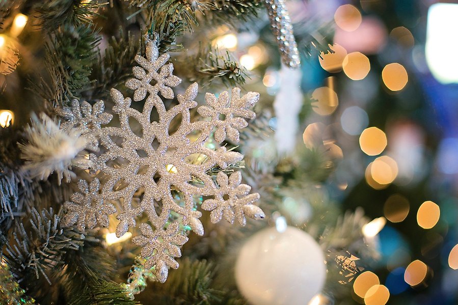 I en julgran hänger en vit snöflinga. Längre bort i bilden syns en vit julgranskula samt ljus.