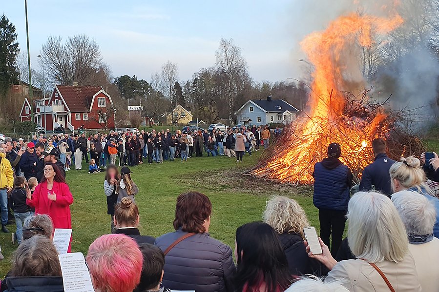 Barn och vuxna står och tittar på en brinnande valborgsbrasa i Munkedals Folkets park på Valborgsmässoafton.