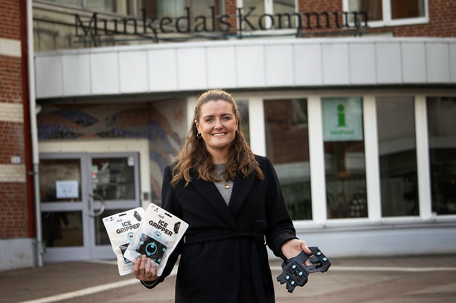 En kvinna står framför en byggnad och håller upp broddar som man sätter på skorna.