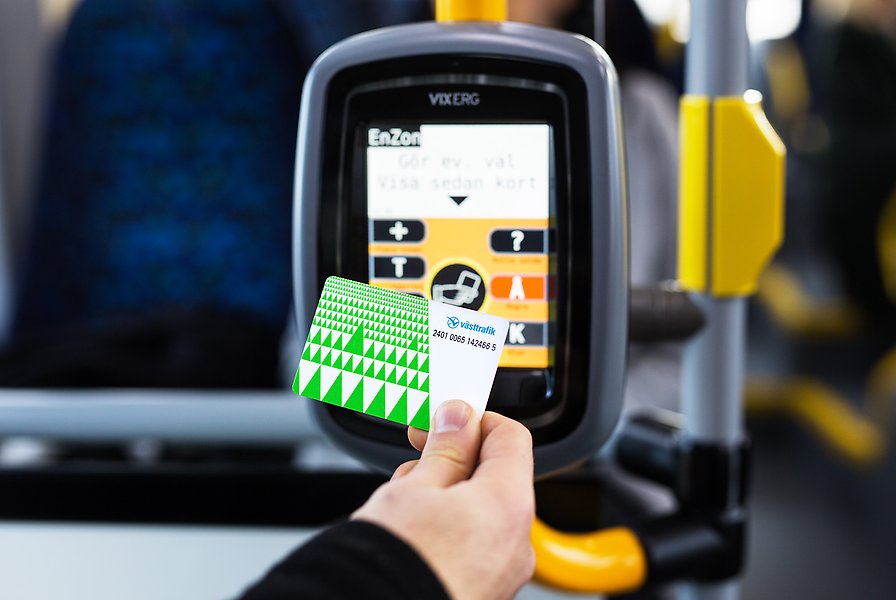 En hand som håller upp ett busskort framför en kortläsare ombord på en buss.