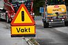 En trafikskylt med texten vakt, i bakgrunden arbetsfordon på en väg.