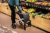 Kvinna med rullator handlar frukt i affär.