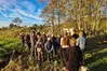 En grupp människor som står utomhus och lyssnar på en person som talar. 