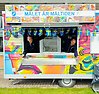 En foodtruck målad i glada färger. Två personer sträcker glatt ut sina armar ur luckorna. Längs med vagnen hänger vimplar med svenska flaggor. På en skylt står det Målet är måltiden tillsammans med Munkedals kommuns och Foodfluencers logotyper.