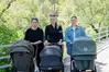 Tre unga kvinnor som står med barnvagnar. I bakgrunden grönskande skog.