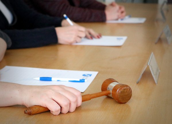 Foto på tre personers händer som sitter vid ett presidiebord. En person håller en ordförandeklubba.
