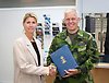 Två personer skakar hand varav en har militäruniform och en bok i handen