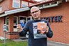 En man som håller upp ett bibliotekskort och böcker. Han står utanför ett bibliotek som ligger i en tegelbyggnad.