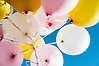 Ett stort knippe ballongen i ljusrosa, vit, gul och guld mot en klarblå himmel.