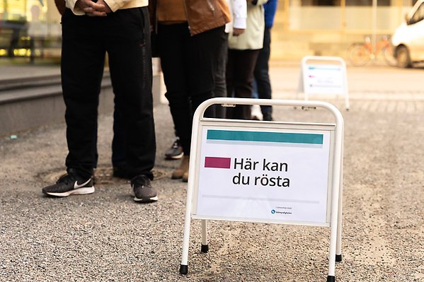 Människor som står på rad vid en skylt om att man kan rösta här